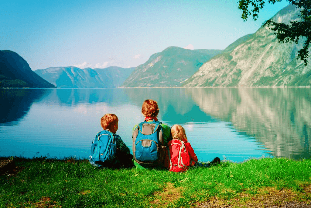 Family walking a quiet Nordic beach beneath green cliffs and evening light.
