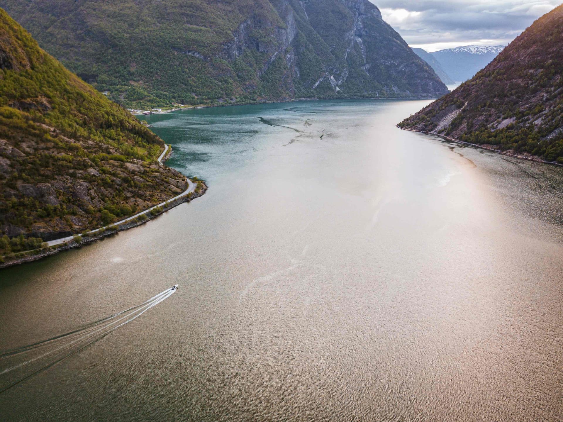 Fjord boat cruising between steep green slopes on a calm afternoon.