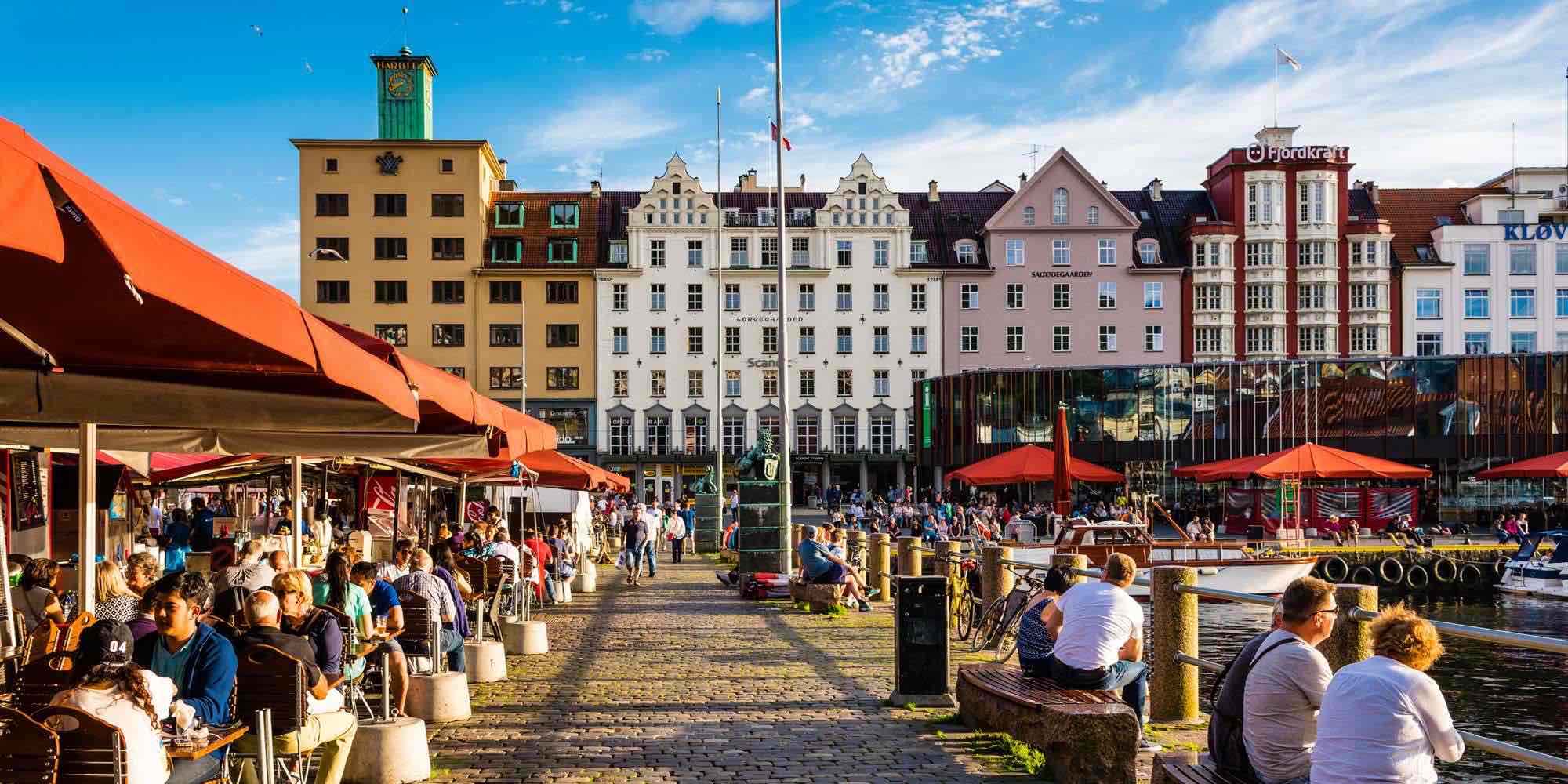 Busy Bergen fish market with open-air cafés and red canopies by the harbor.